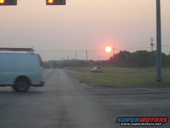 White van driving on road at sunset, distant SUV in grassy field