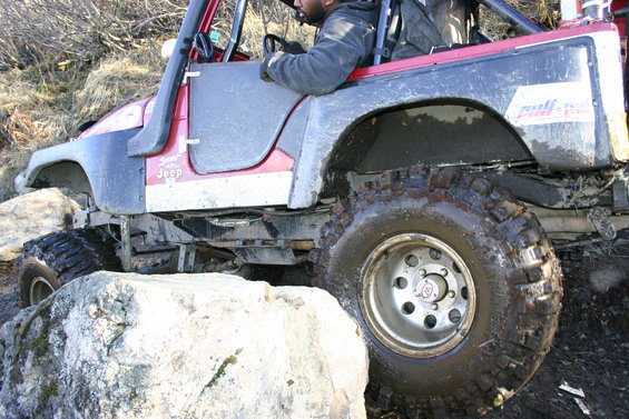 Jeep TJ off-roading over rocks. Driver is visible behind the wheel