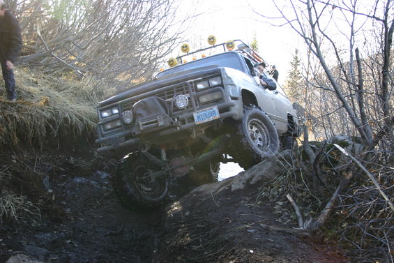 Off-road truck with lifted suspension and large tires navigating a muddy incline