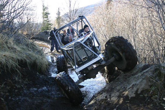 Off-road buggy with a roll cage navigating a muddy, rocky trail with two people inside