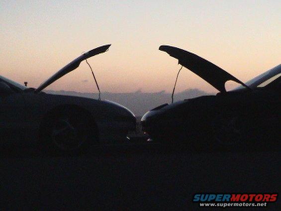 two cars facing each other with hoods open at sunset