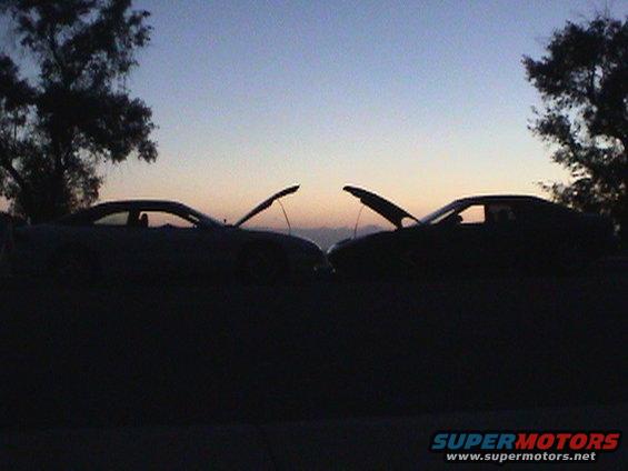 Two dark coupes with hoods open face each other at dusk