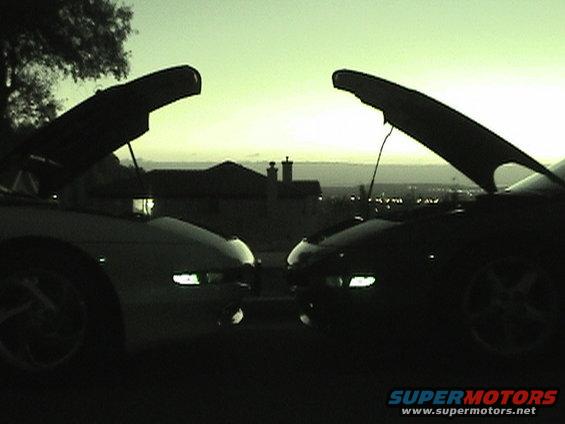 Two cars with hoods open, facing each other at dusk