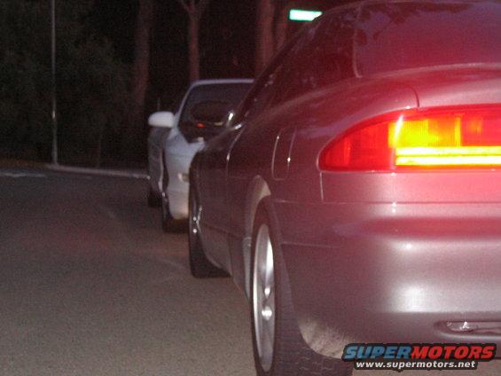 Dark gray coupe from rear, parked behind a white sedan. Visible taillight and wheel