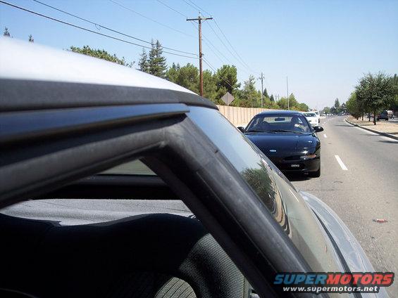 Black 1993 Ford Probe driving on a sunny day, seen from another car