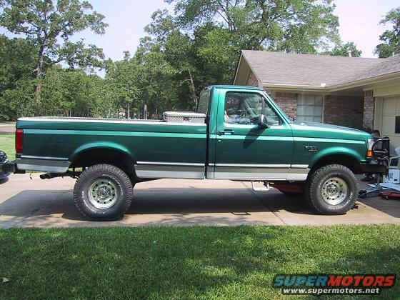 Green pickup truck parked in driveway, side view. Has a toolbox in the bed