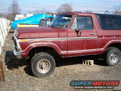 Maroon Ford Bronco parked outside with a blue tarped object behind it