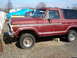 1979 Ford Bronco - This maroon Ford Bronco is parked on gravel with a cinder block supporting the frame.