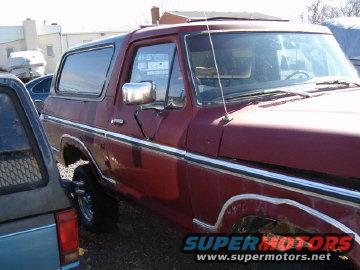 Red 1978 Ford Bronco with chrome trim and a dark blue vehicle to its left