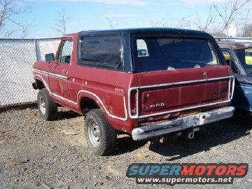 1978 Ford Bronco rear 3/4 view, red with black top. Another vehicle partially visible to the right