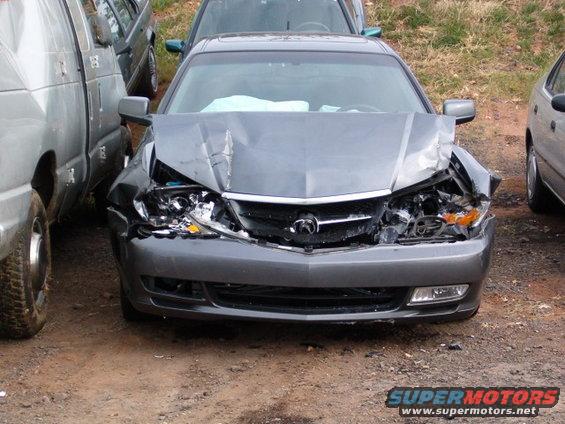 Front view of a wrecked 2003 Acura TL, parked between a van and another car
