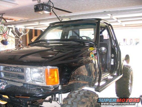 Black Toyota truck, 3/4 front view, modified with large tires and roll cage