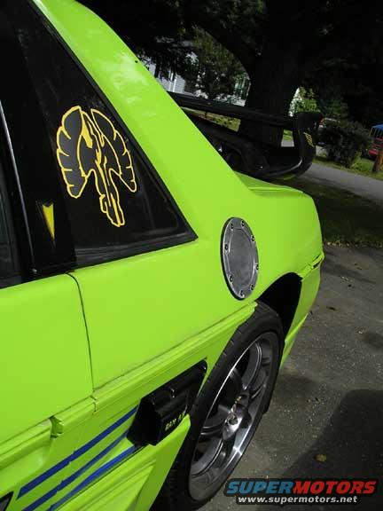 Lime green 1984 Pontiac Fiero with a black spoiler and a yellow winged emblem on the rear quarter window