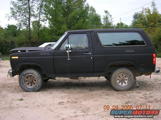 Black 1980s Ford Bronco parked on dirt, hood up, side view