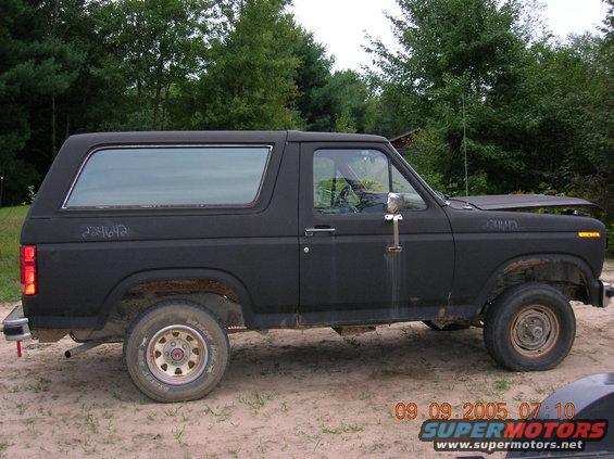 Black 1980s Ford Bronco, side view, hood up, flat tire, rust on wheel wells