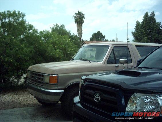 Tan 1987 Ford Bronco parked next to a black Toyota Tacoma