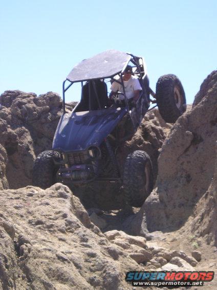 Off-road buggy with roll cage climbing over large rocks on a sunny day