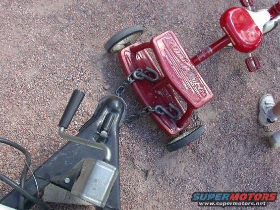 Red Radio Flyer wagon chained to a trailer hitch on gravel