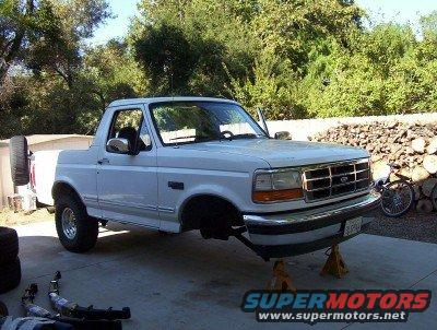 White Ford Bronco on jack stands, front end raised, spare tire mounted on rear