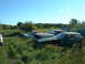 1978 Ford Mustang II - A collection of abandoned vehicles sits in a grassy field under a clear blue sky.