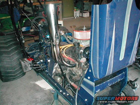 Blue custom tractor with exposed engine, large rear tire, and chrome exhaust pipes