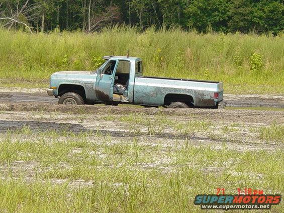 Light blue pickup truck stuck in mud, driver's door open