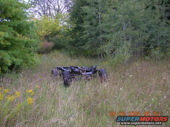 Vehicle frame and chassis with wheels sitting in tall grass and weeds