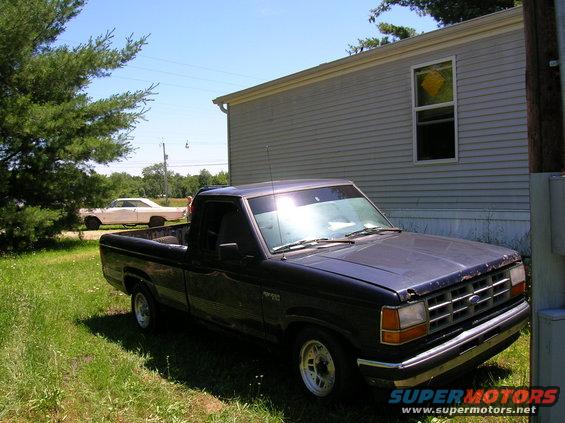 Dark blue pickup truck parked in front of a mobile home, with a white classic car in the background