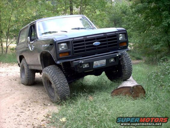Dark blue 1986 Ford Bronco with lifted suspension driving over a log