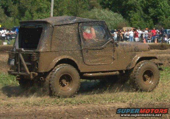 Muddy Jeep driving through a dirt track with spectators in the background