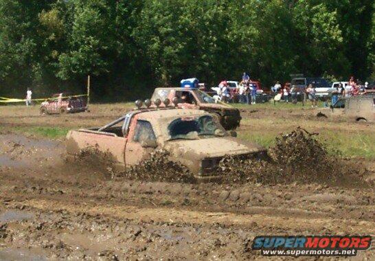 Trucks stuck in a mud bog with spectators in the background