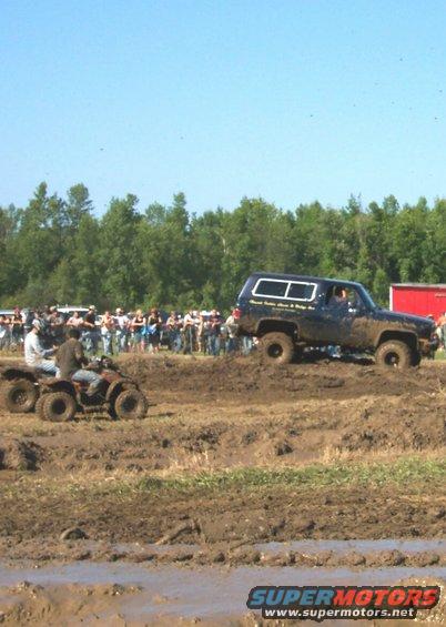 Muddy SUV and ATVs at a mud bogging event with a crowd watching