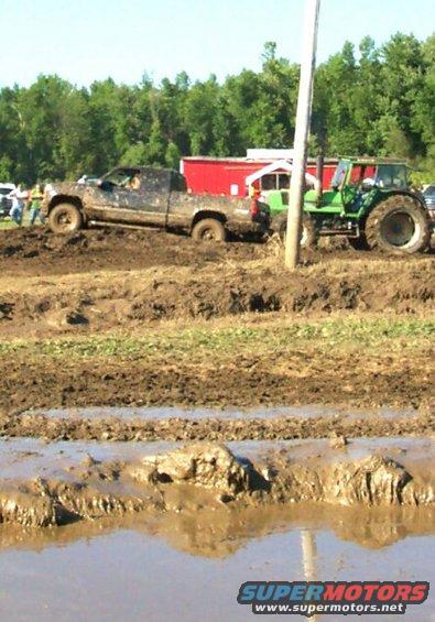 Muddy pickup truck stuck in a field next to a green tractor