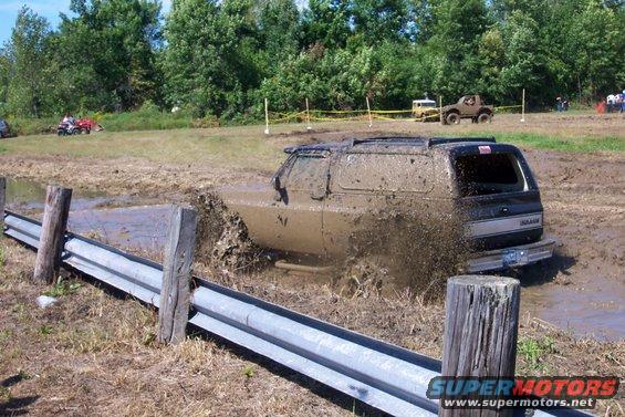 SUV stuck in mud pit, splashing water. Another off-road vehicle visible in background