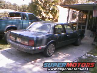 Dark sedan, rear view, parked next to a pickup truck