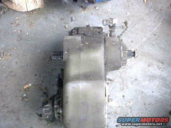 Gray transfer case with splined shafts on both ends, resting on a concrete floor