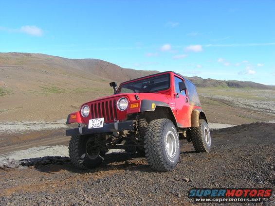Red 2001 Jeep TJ on a dirt road, front 3/4 view, with off-road tires and snorkel
