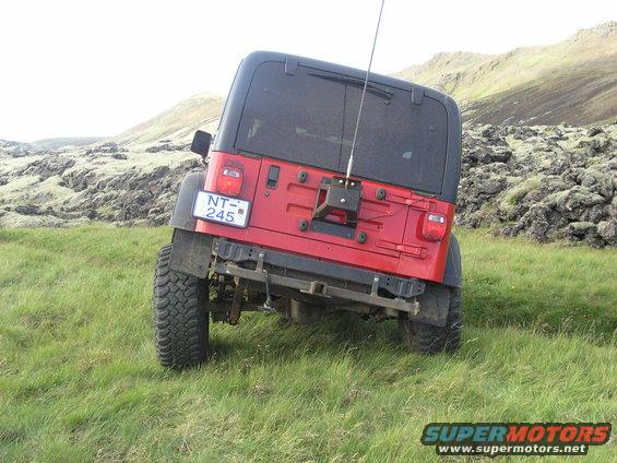Red Jeep Wrangler parked on a grassy hill with rocky terrain in the background. License plate NT-245 is visible
