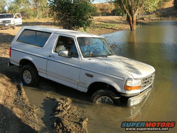 1994 Ford Bronco stuck in mud and water, another white truck visible in background