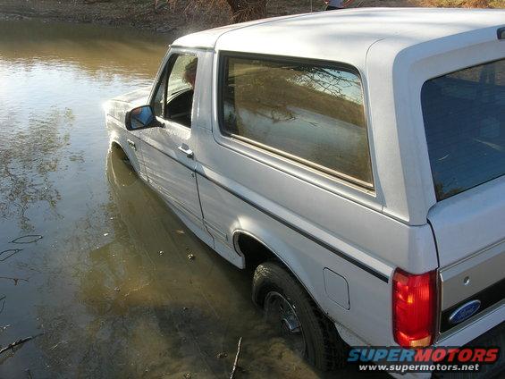 1994 Ford Bronco partially submerged in muddy water, side view