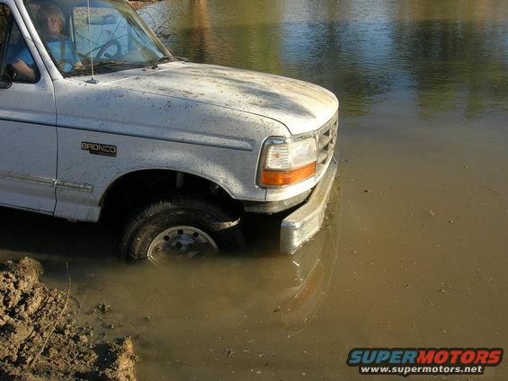White 1994 Ford Bronco stuck in mud and water, 'BRONCO' badge visible