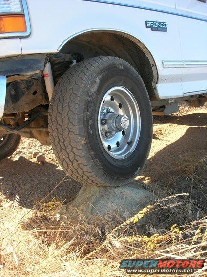 White Ford Bronco side view, front wheel on rock. Blue Bronco badge visible