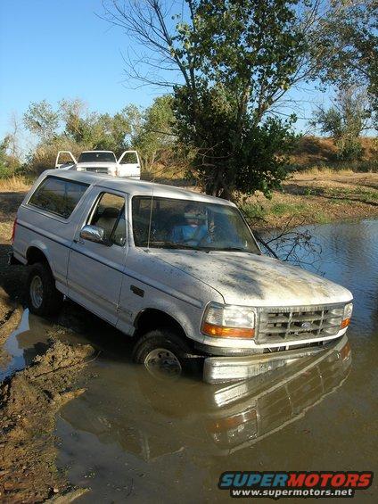 White 1994 Ford Bronco stuck in mud and water, front grille visible