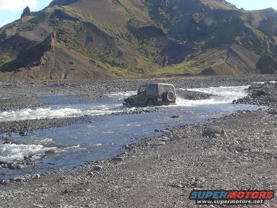Jeep TJ driving through a rocky riverbed with mountains in the background