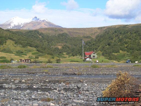 Rural scene with snow-capped mountain, buildings, and a blue tractor in the distance