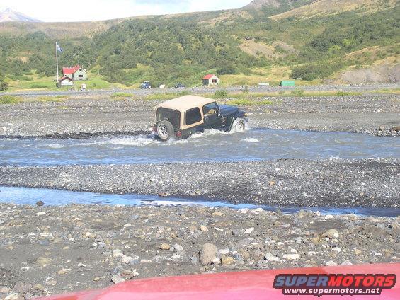 Jeep TJ driving through a rocky stream with a tan soft top