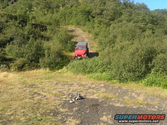 Red 2001 Jeep TJ on a dirt road surrounded by greenery