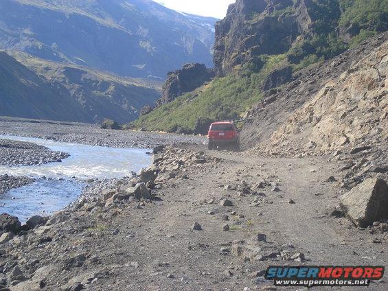 Red SUV on a rough dirt road next to a river in a mountain valley