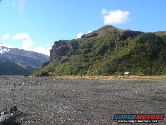 Rocky terrain with mountains and vegetation under a blue sky with clouds