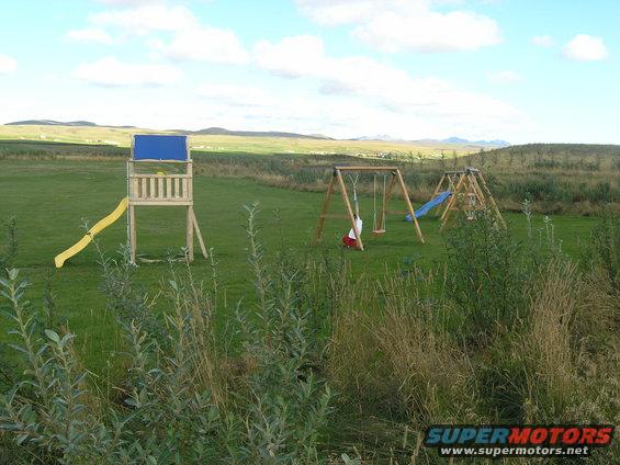 Wooden playground structure with yellow slide, swings, and blue slide on a grassy field